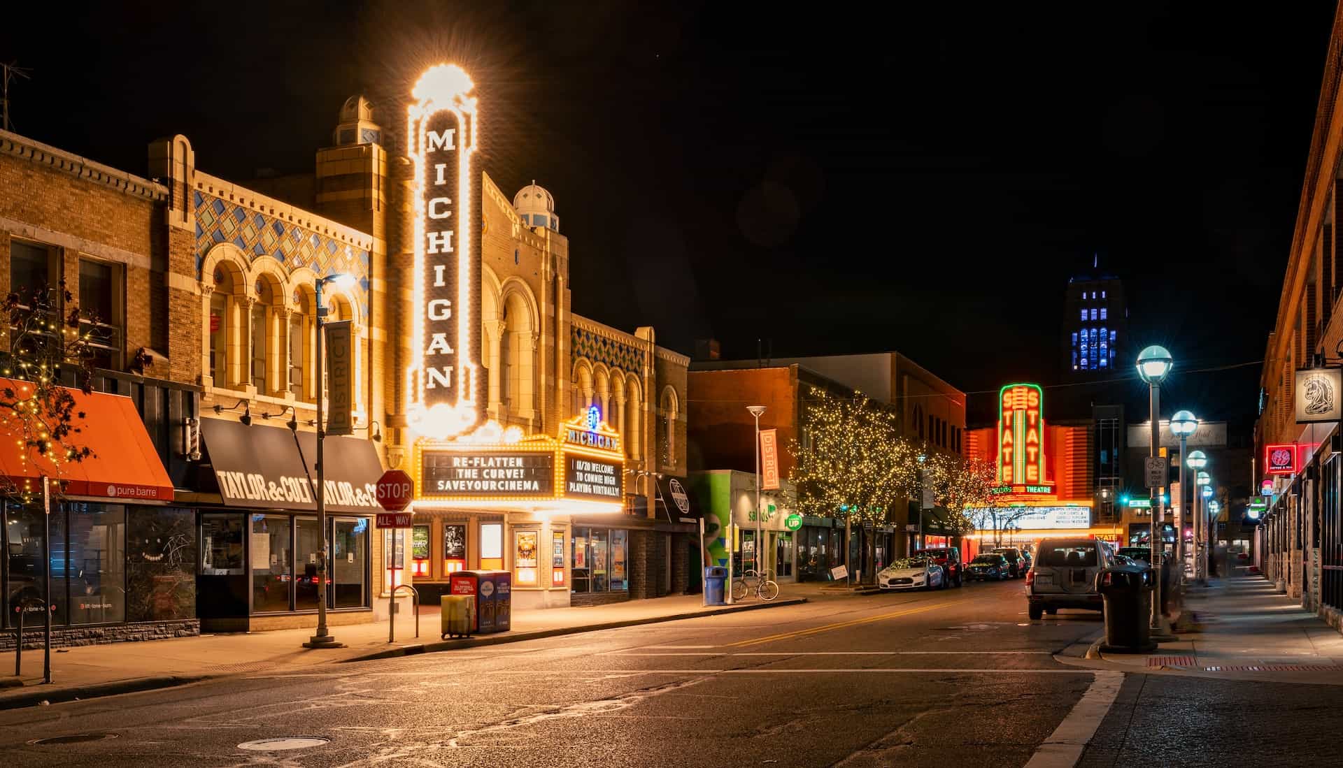 Main Street in a small town in Michigan, United States of America, featuring several storefronts and the bright, lit-up marquee of the town’s local cinema.