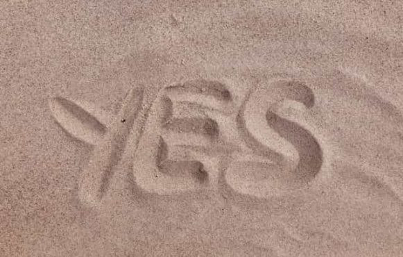 The word “yes” drawn into the sand on a beach or in a desert.