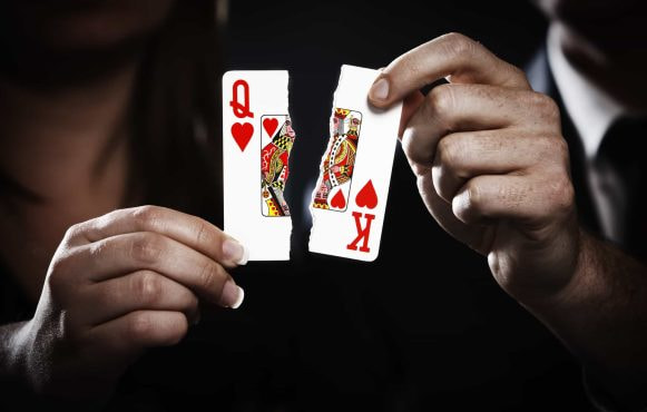 Playing cards, a Queen and King of Hearts, are torn in two.