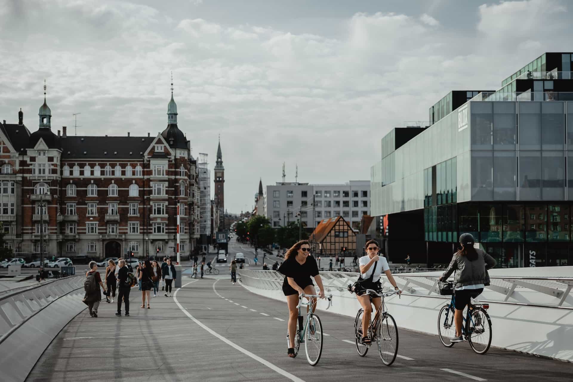 People cycling and walking on a path near buildings.