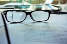 A pair of glasses resting atop a pile of paperwork placed on a table.