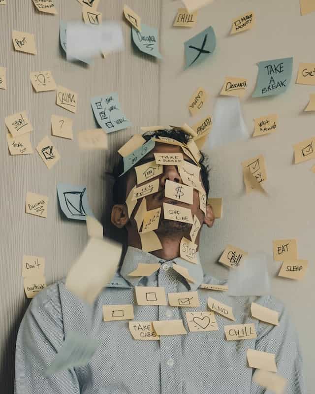 A man leaning against a wall, both of which are covered in dozens of post-it notes with various life affirmations and motivational slogans.