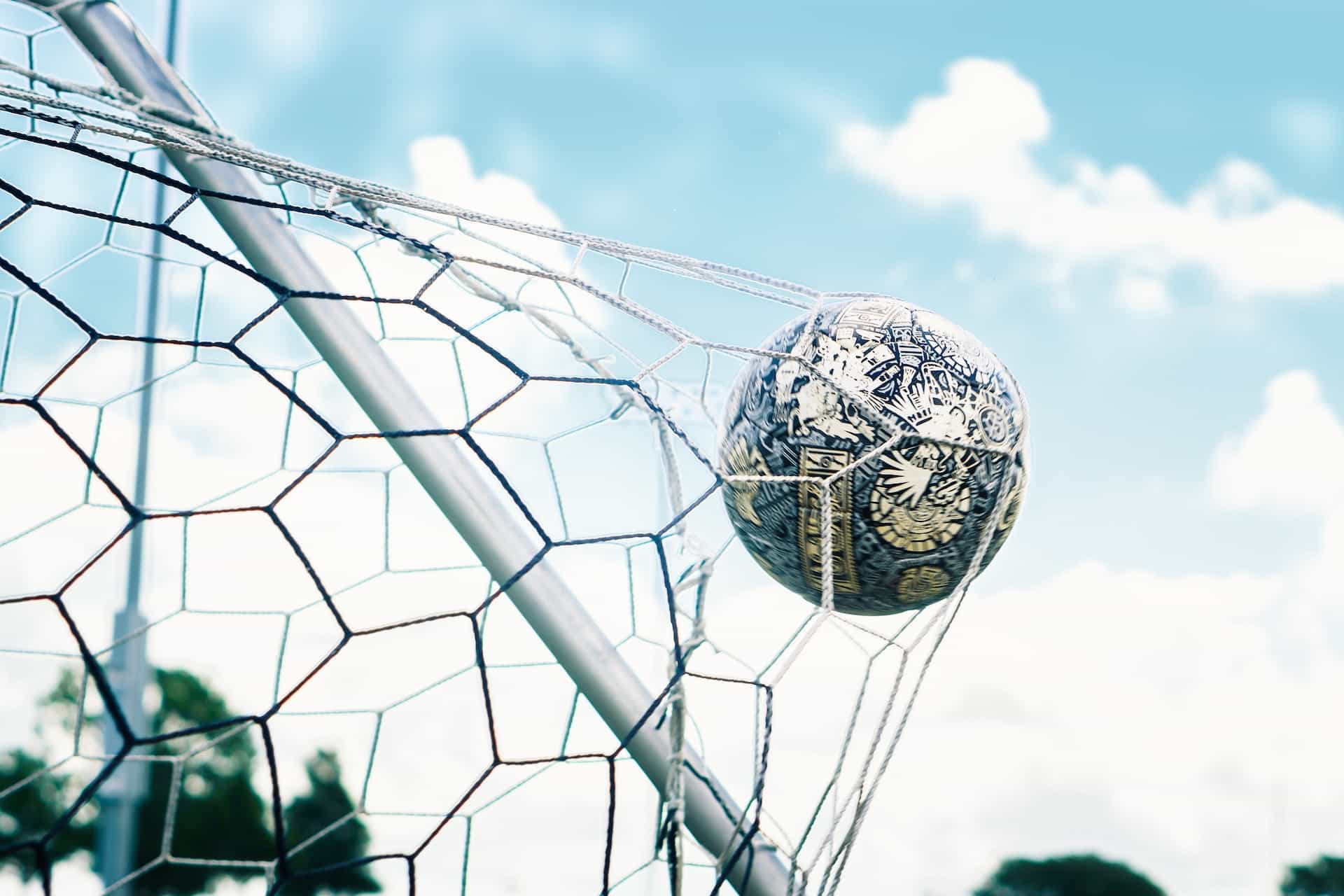 A soccer ball going into a goal net.