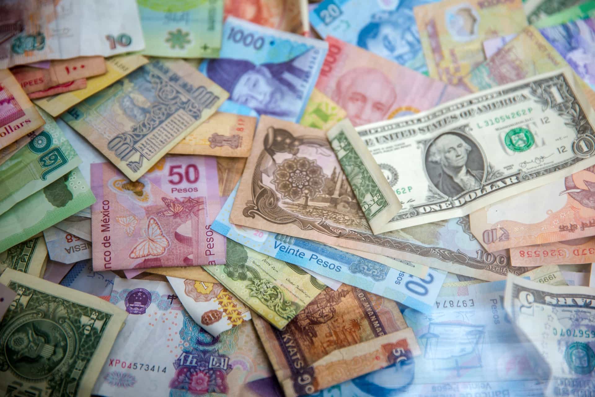 Various colorful currencies displayed on a flat surface with a $1 USD bill on top.