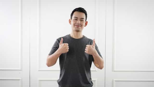 A man gives a sign of two thumbs up towards the camera.