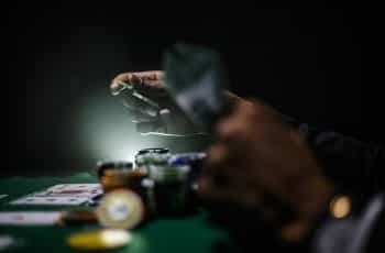 A person’s hands playing a pair of poker chips during a game of poker at a physical poker table.