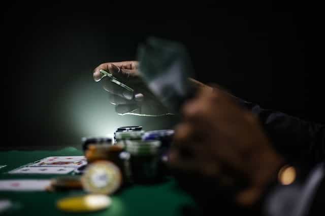 A person’s hands playing a pair of poker chips during a game of poker at a physical poker table.