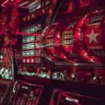 A series of classic roulette machines drenched in neon red light inside of an indoor retail casino location.