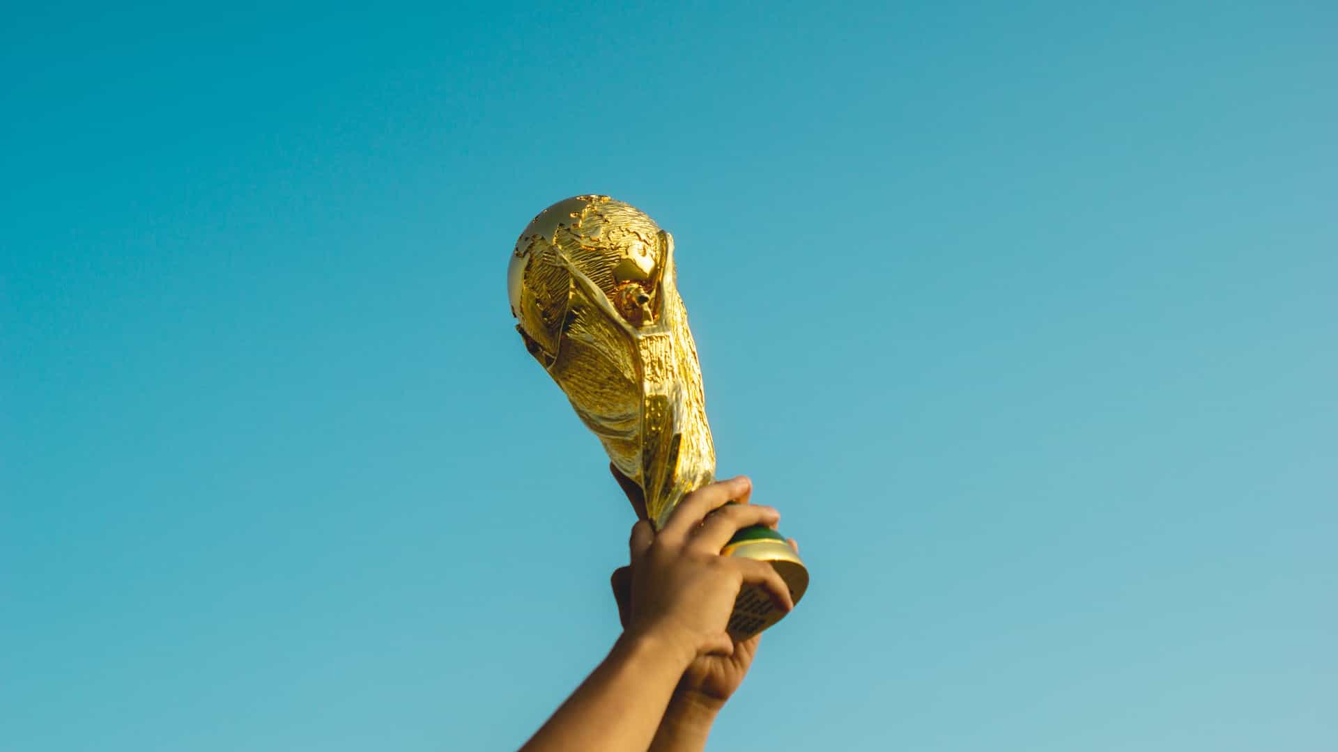Hands hold the World Cup trophy up against a bright blue sky.