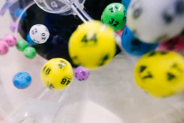 Many multi-colored lottery balls fly around a container.