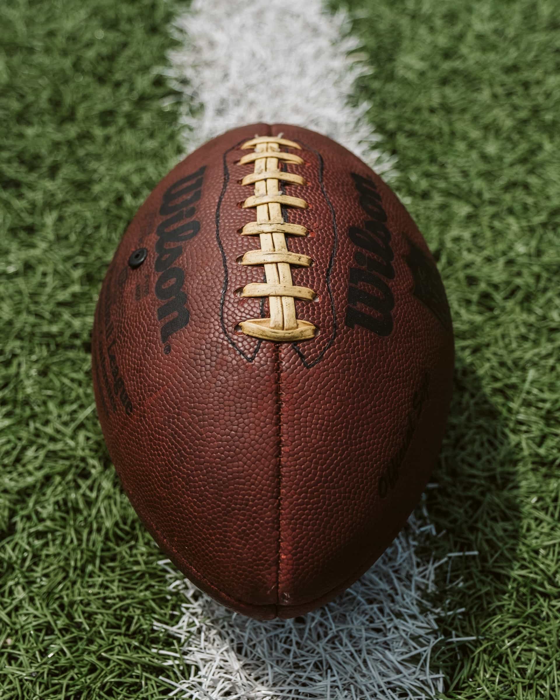 An American football with its iconic ribbed spine sitting on a pitch before a game.
