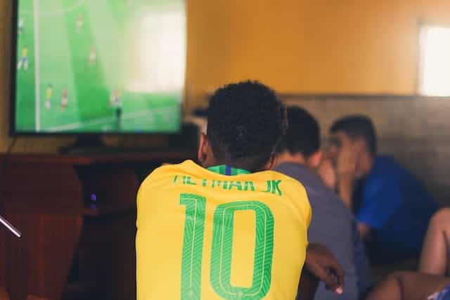 A man wearing a Brazilian soccer jersey watches a game on the television.