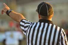 A referee in a striped uniform holds on his arm to signal to players.
