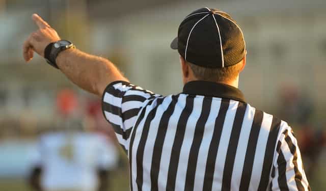 A referee in a striped uniform holds on his arm to signal to players.