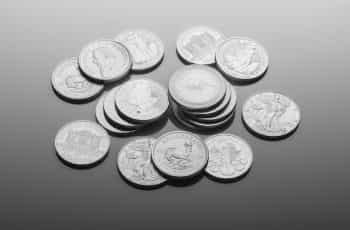 Numerous silver coins of varying currencies lying flat on a table.