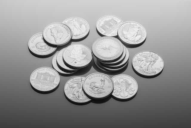 Numerous silver coins of varying currencies lying flat on a table.