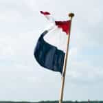 A red, white, and blue flag against a pale blue sky.