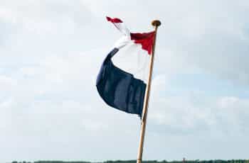 A red, white, and blue flag against a pale blue sky.