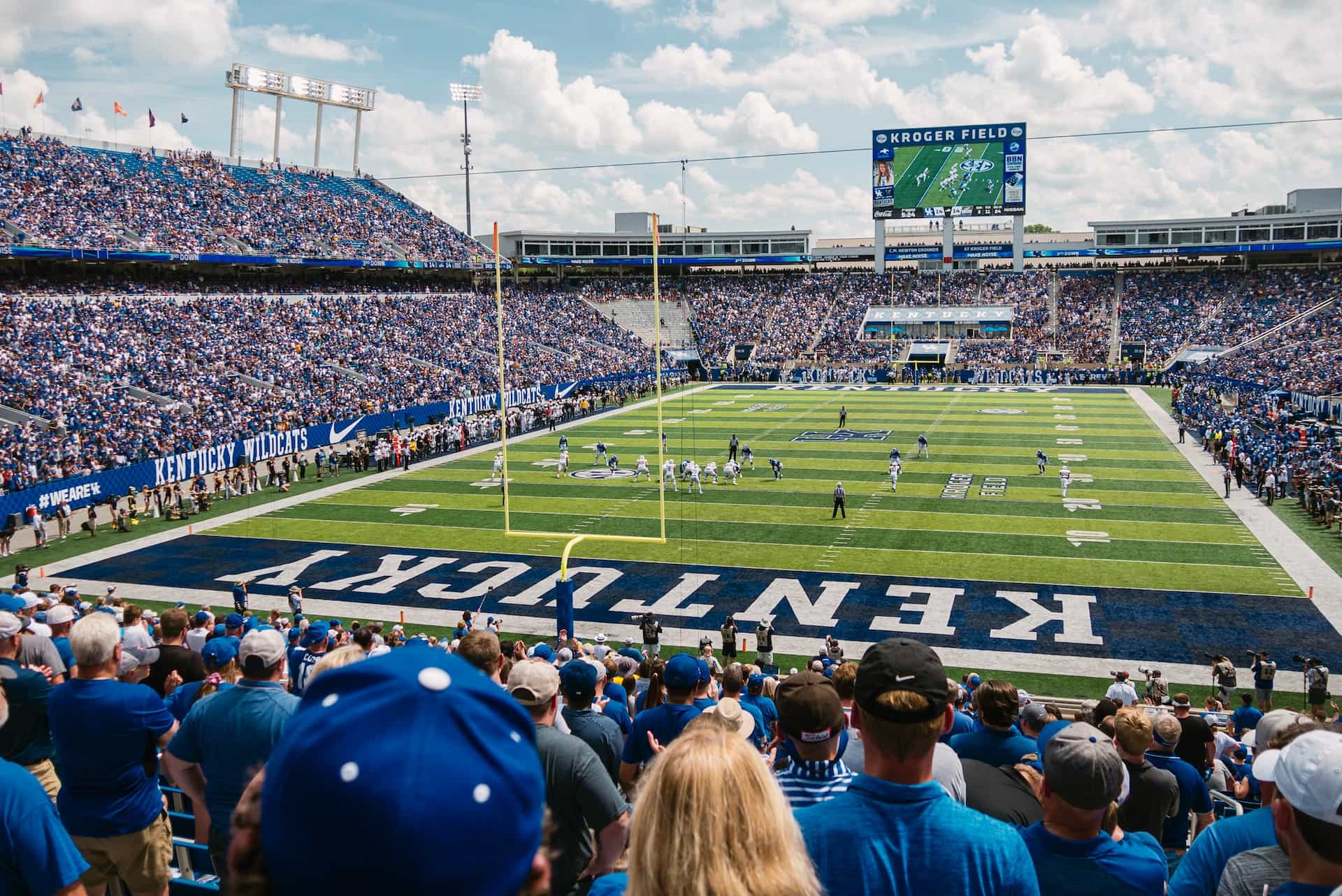 The inside of an American football stadium in the state of Kentucky during a big game, featuring thousands of spectators in the stands and two teams on the field.