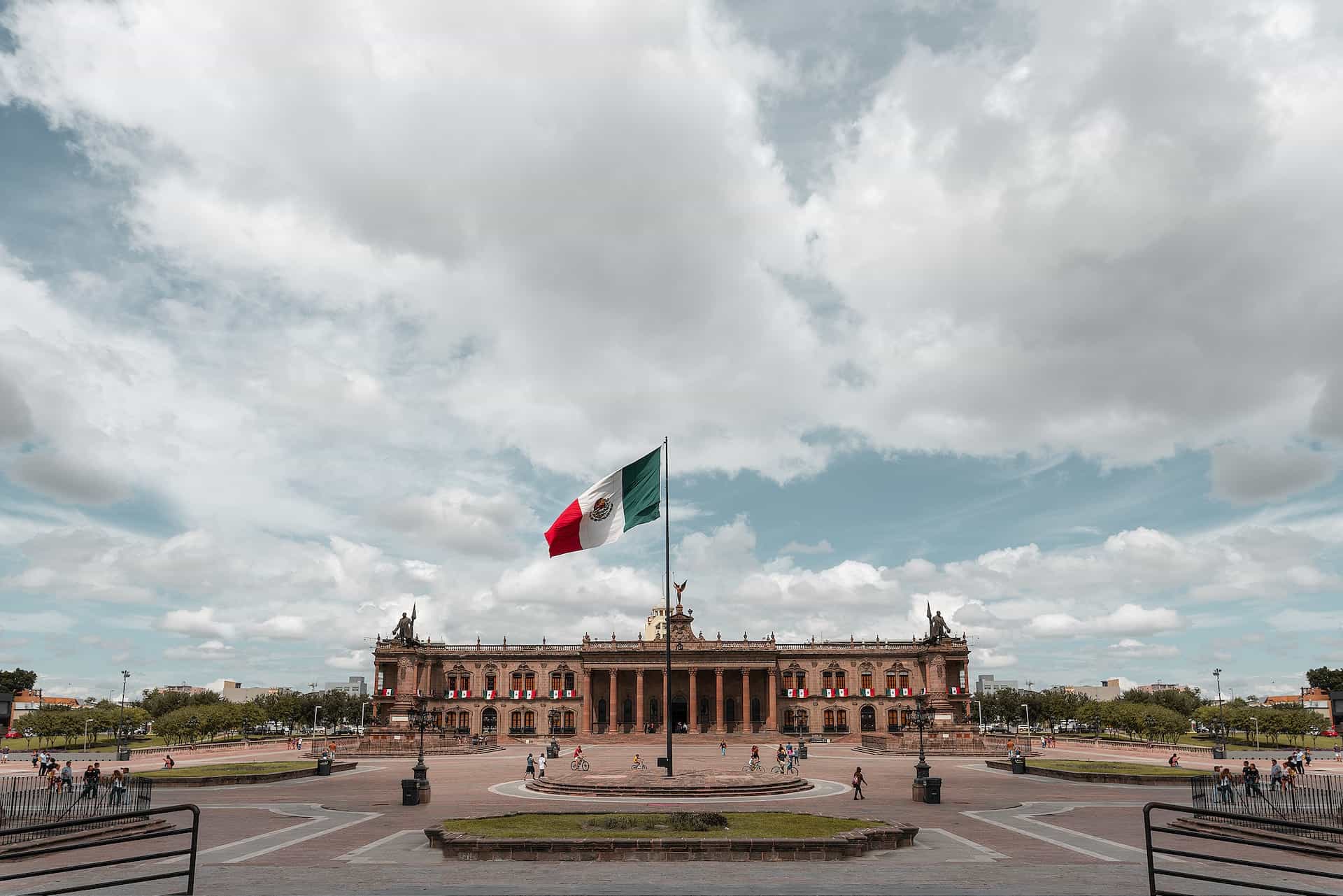 A Mexican flag waves about a prominent government building with columns on a plaza in Monterrey, Mexico.