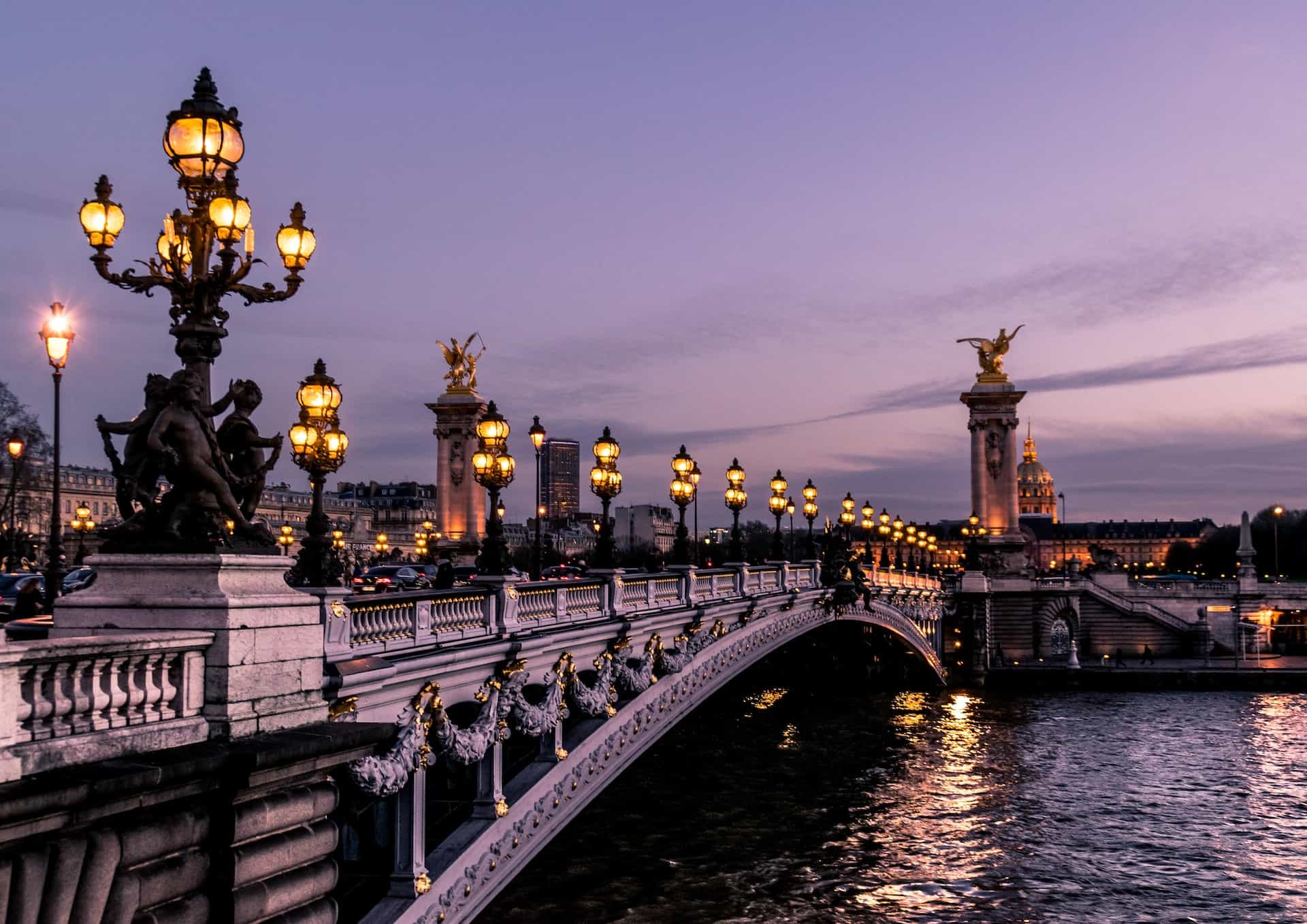 A Parisian bridge with lit lamp posts over water.