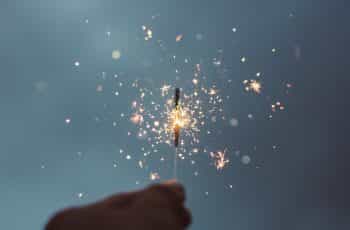 A hand holds a sparkler light emitting sparks.