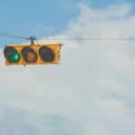 A horizontal traffic light hanging high up in the air while displaying a green light for “go”.