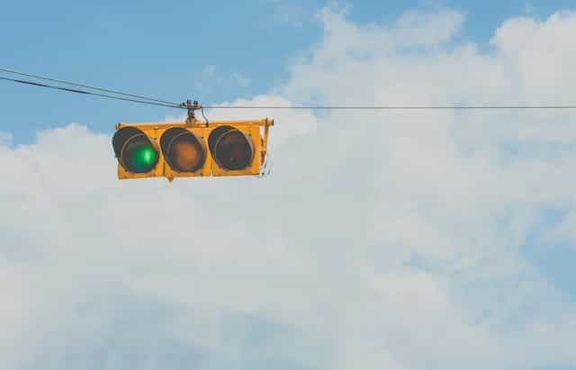 A horizontal traffic light hanging high up in the air while displaying a green light for “go”.