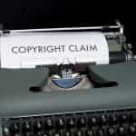 An old-fashioned typewriter sitting on a table, with the words “Copyright Claim” written in large font on the sheet of paper sticking out of the machine.