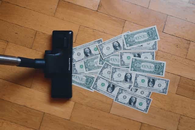 A vacuum cleaner about to suck up several US dollar bills off the floor.
