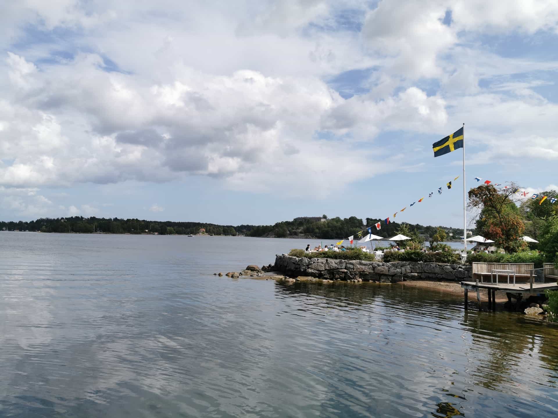 A flag hoisted on land near a huge water body.