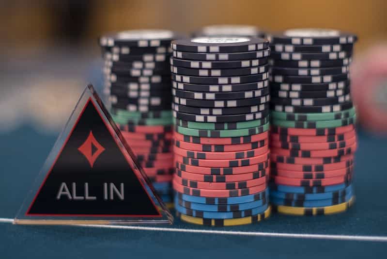 Chips and an ‘All IN’ dealer button on a poker table.