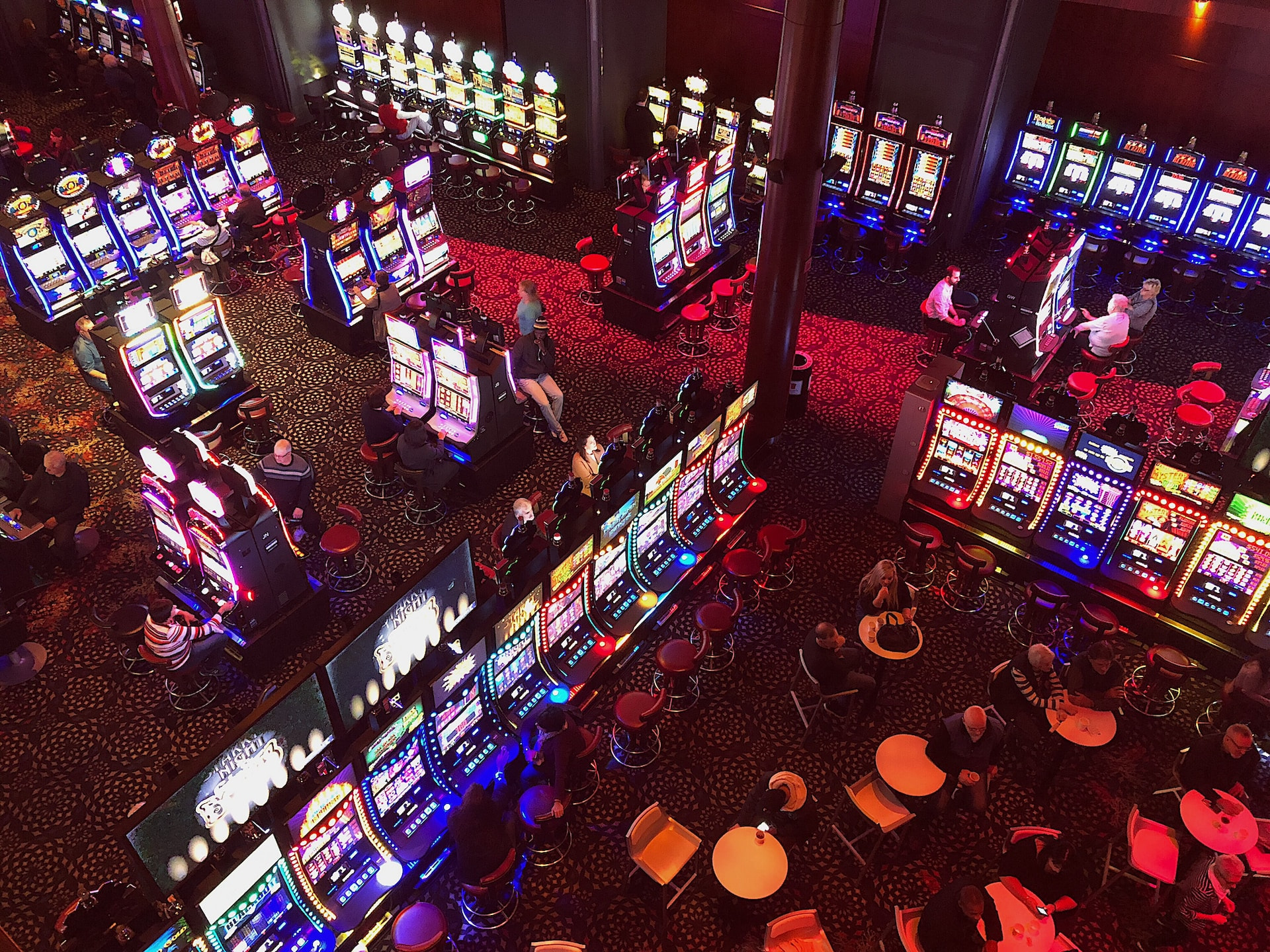 An overhead view of a casino floor, featuring dozens upon dozens of lit-up video slot machines, with a handful of players scattered around.