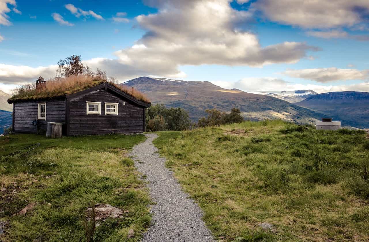 A black and brown house on a green hill with a pathway.