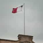 A red and white flag against a cloud sky.