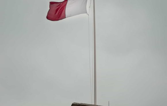 A red and white flag against a cloud sky.