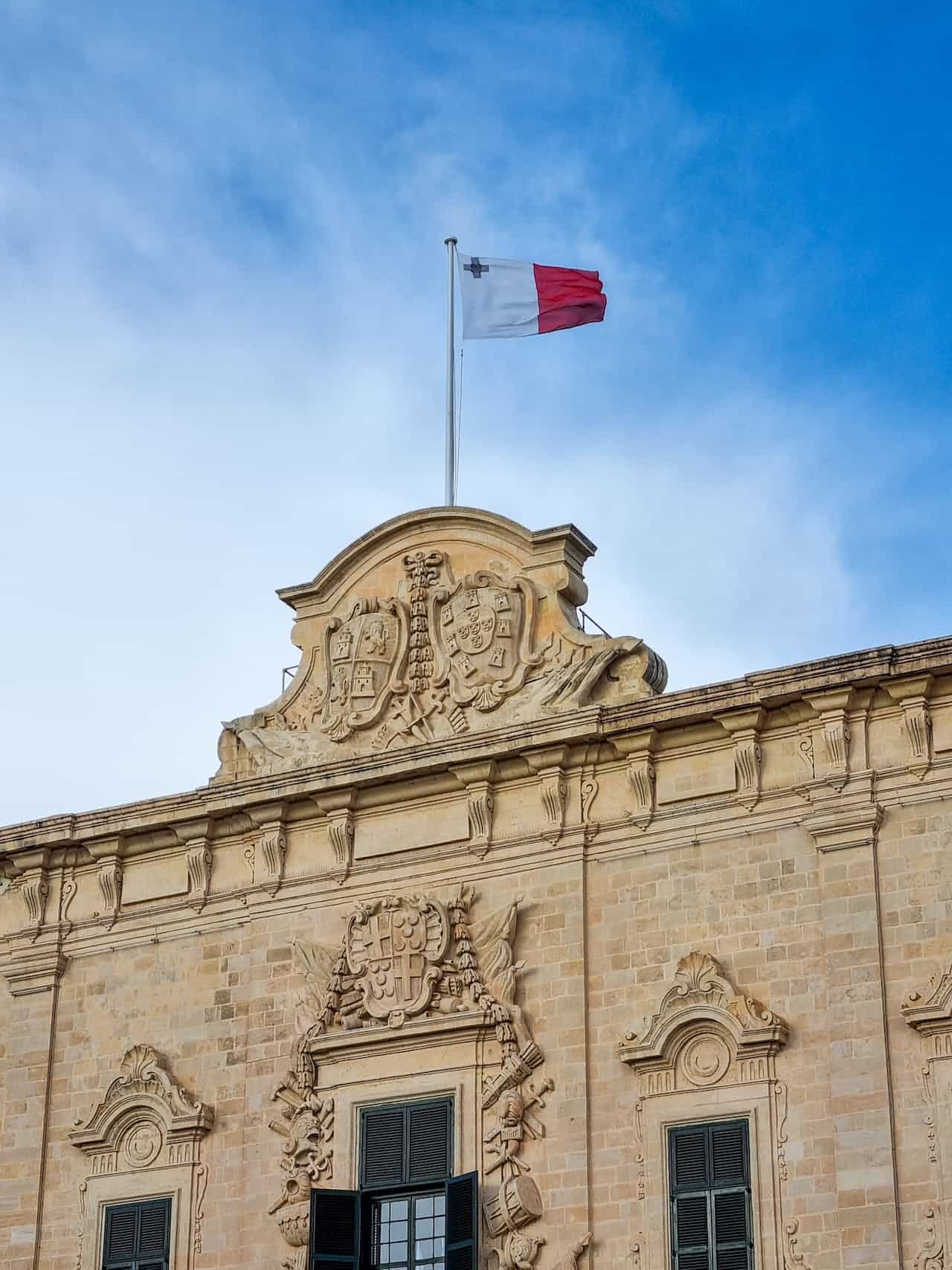 A white and red flag hoisted on a building against a blue sky.