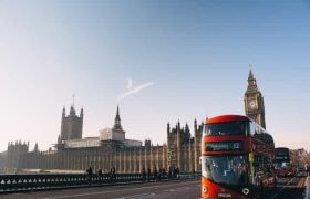 A red bus passing across the bridge in front of Westminster in London, UK.