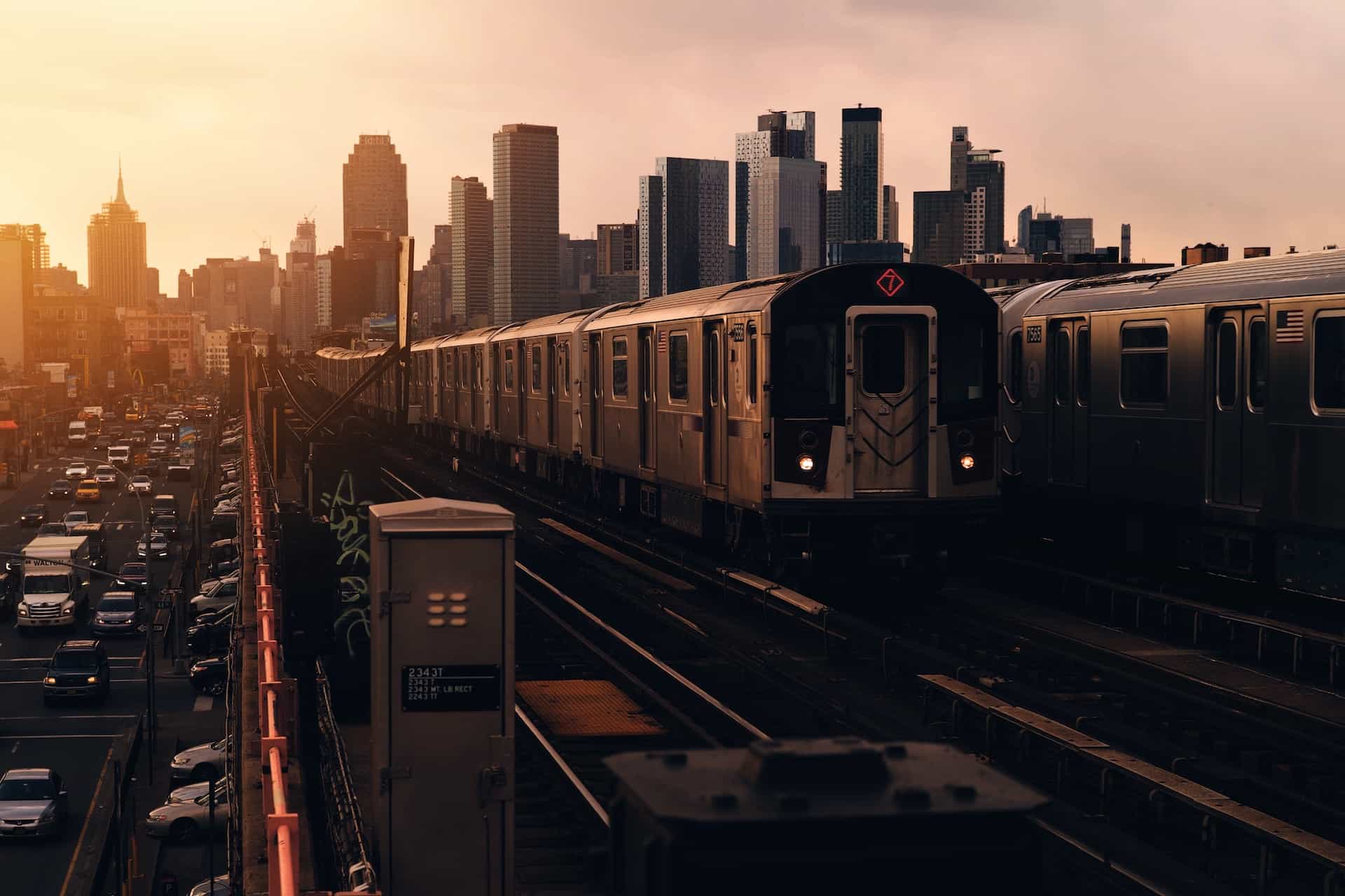 The 7 train in the New York subway system riding overground away from the island of Manhattan into the borough of Queens while the sun sets in the background.