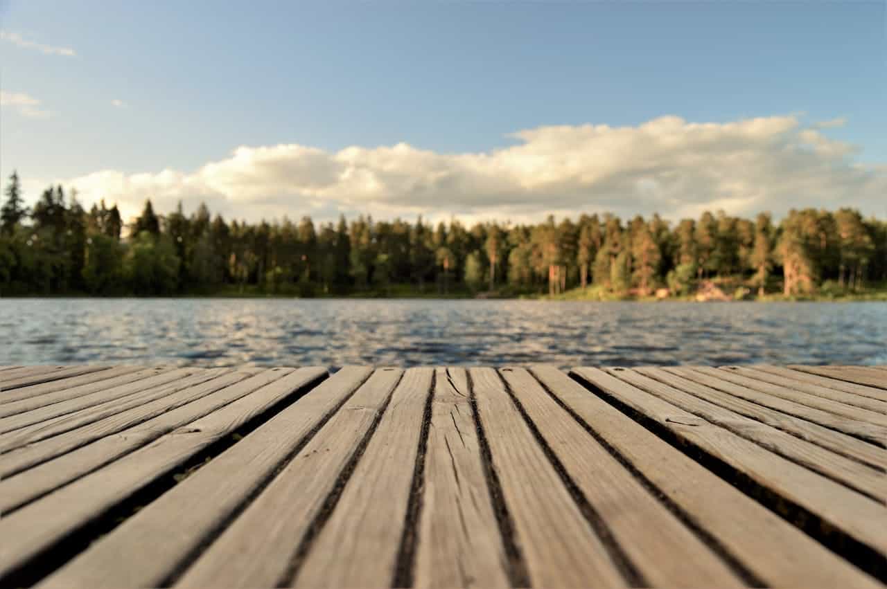 The view of a water body, trees, and the sky from a wooden surface.