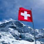 A red flag with a white cross hoisted near a snowy peak
