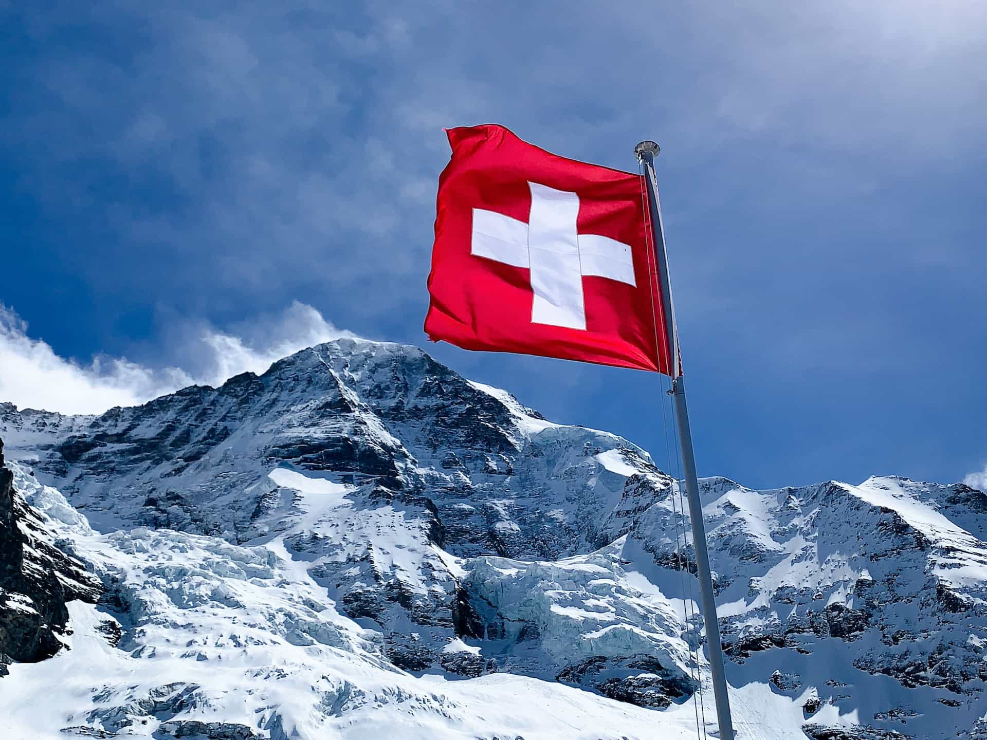 A red flag with a white cross hoisted near a snowy peak