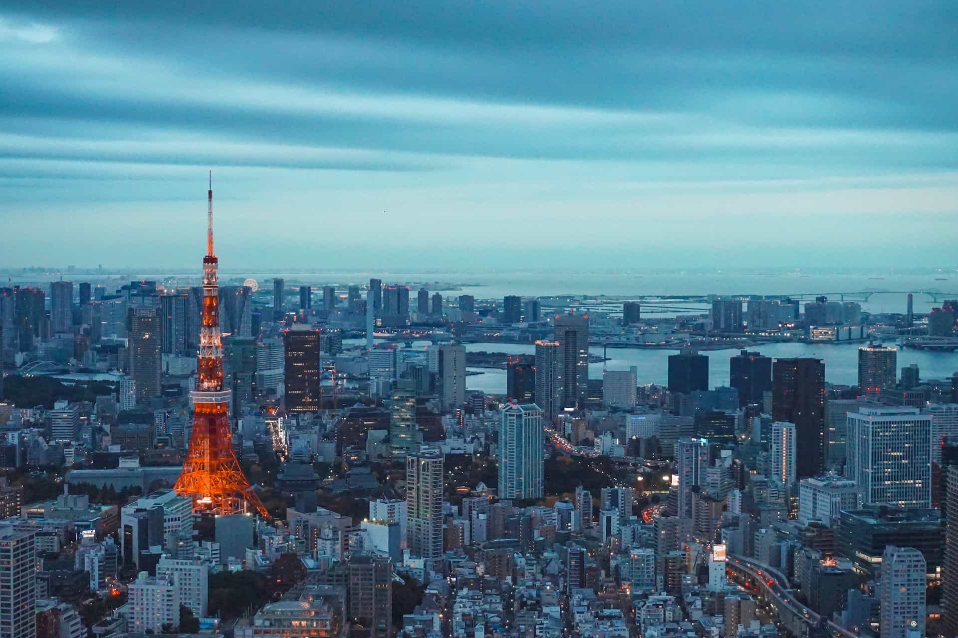 An aerial view of central Tokyo as night begins to fall, featuring endless tall buildings and skyscrapers wrapped around a bay.