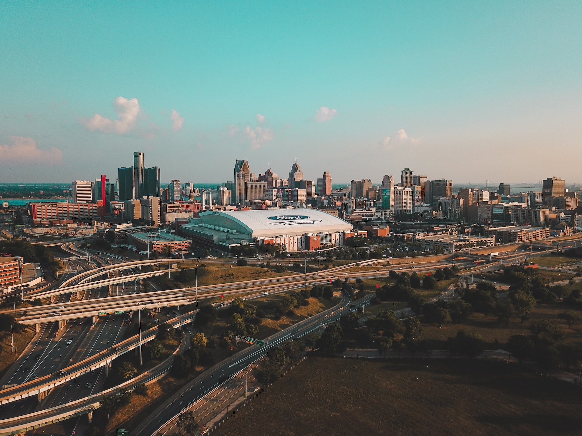 The dense downtown area of Detroit, Michigan, featuring dozens of tall buildings and skyscrapers, as well as a large stadium with the Ford logo on its roof.