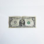 A US Dollar bill lying flat on a white surface, prominently displaying the face of former US President George Washington.
