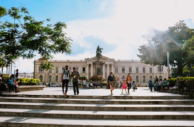 People walk in front of a government building with columns in El Salvador.