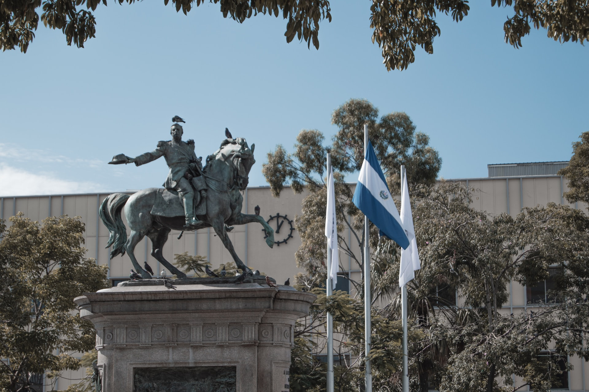 A statue of a man on a horse near the El Salvador flag in a plaza.