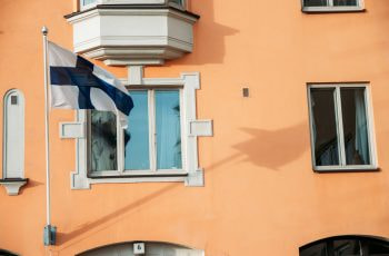 A white and blue flag in front of a window of a brown building.