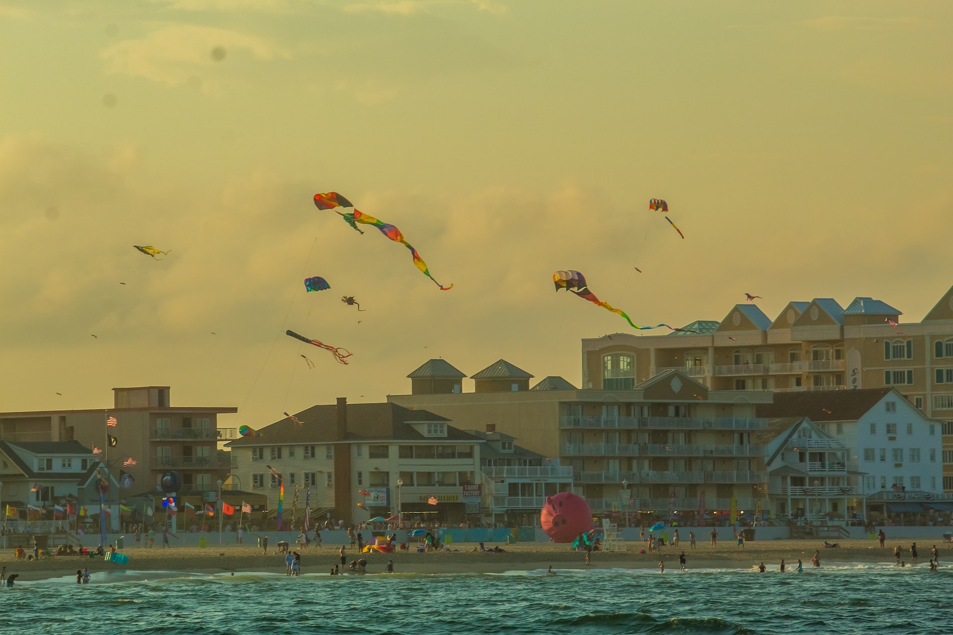 A busy beach in the state of Maryland during the summer, featuring many beachgoers relaxing and flying kites while the sun sets.
