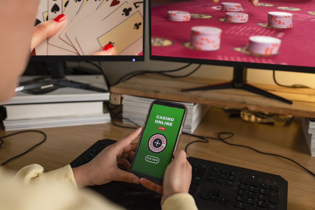 A man looks at his gambling app, where monitors displaying more gambling pastimes can be seen in the background.